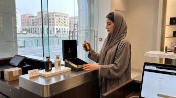 WAJD Fragrances shipping and returns: woman placing a WAJD bottle in its gift box at a Doha boutique checkout counter